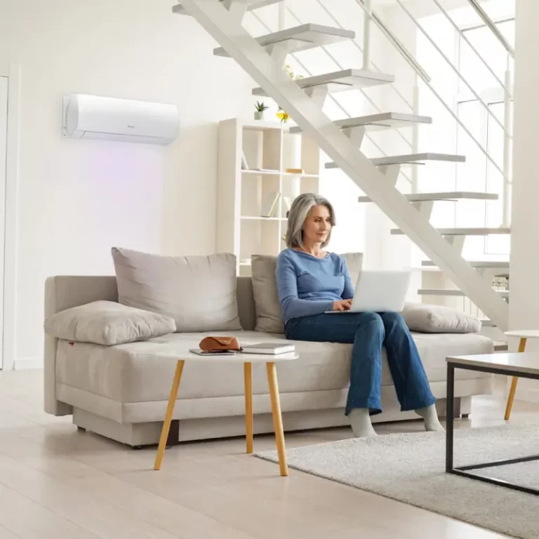 Pompy ciepła Daikin komfortowe w codziennym użytkowaniu. Starsza Pani siedząca na kanapie z laptopem, a za nią na ścianie pracuje klimatyzator Daikin